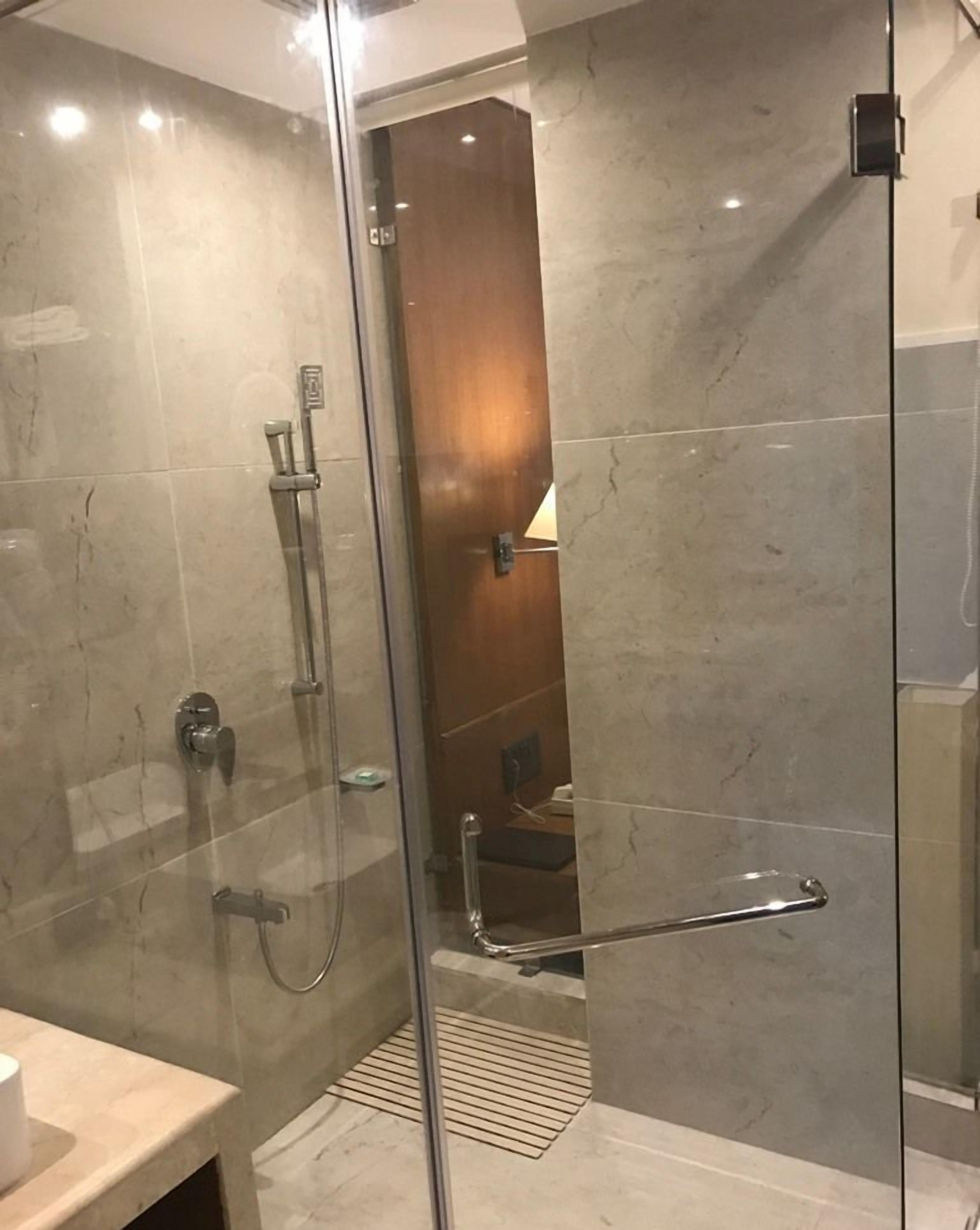 Un baño moderno con cabina de ducha de vidrio, suelo de mármol y puerta de madera que da a un pasillo.