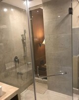 Un baño moderno con cabina de ducha de vidrio, suelo de mármol y puerta de madera que da a un pasillo.