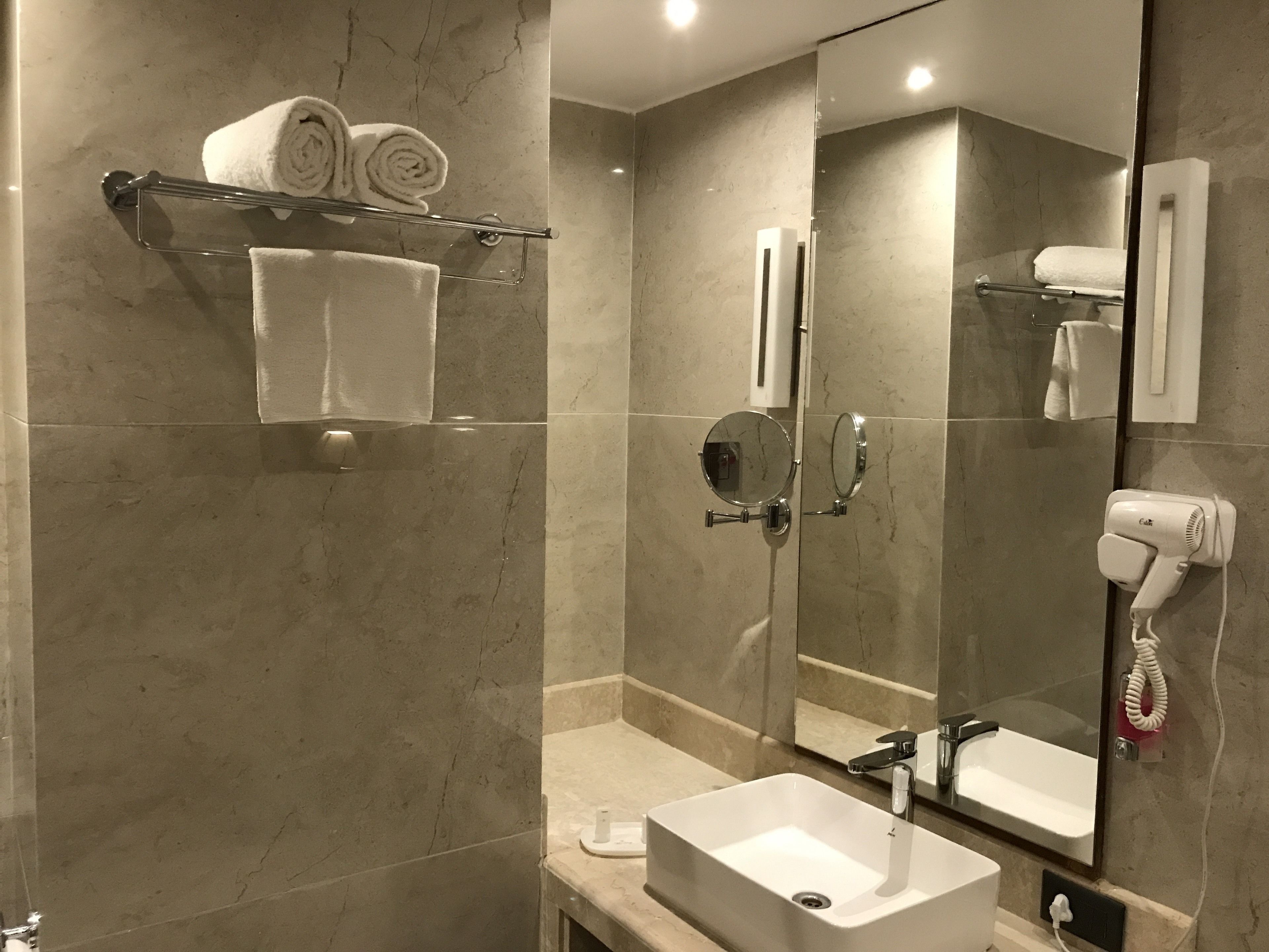Un baño moderno con un espejo grande, un lavabo, un perchero con toallas y un secador de pelo.