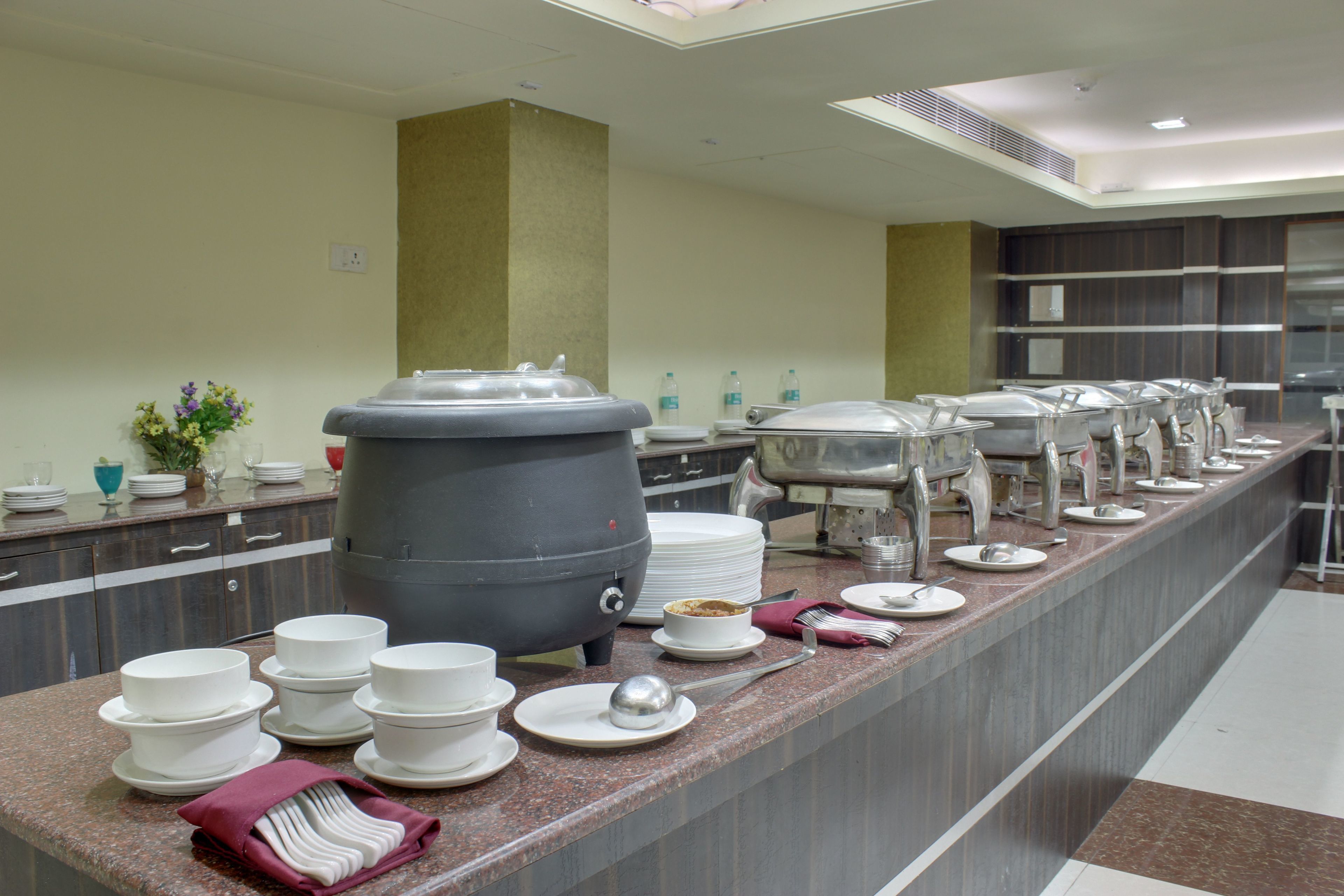 Un buffet avec plusieurs points de service, un grand distributeur de boissons et une variété de plats et d’ustensiles.