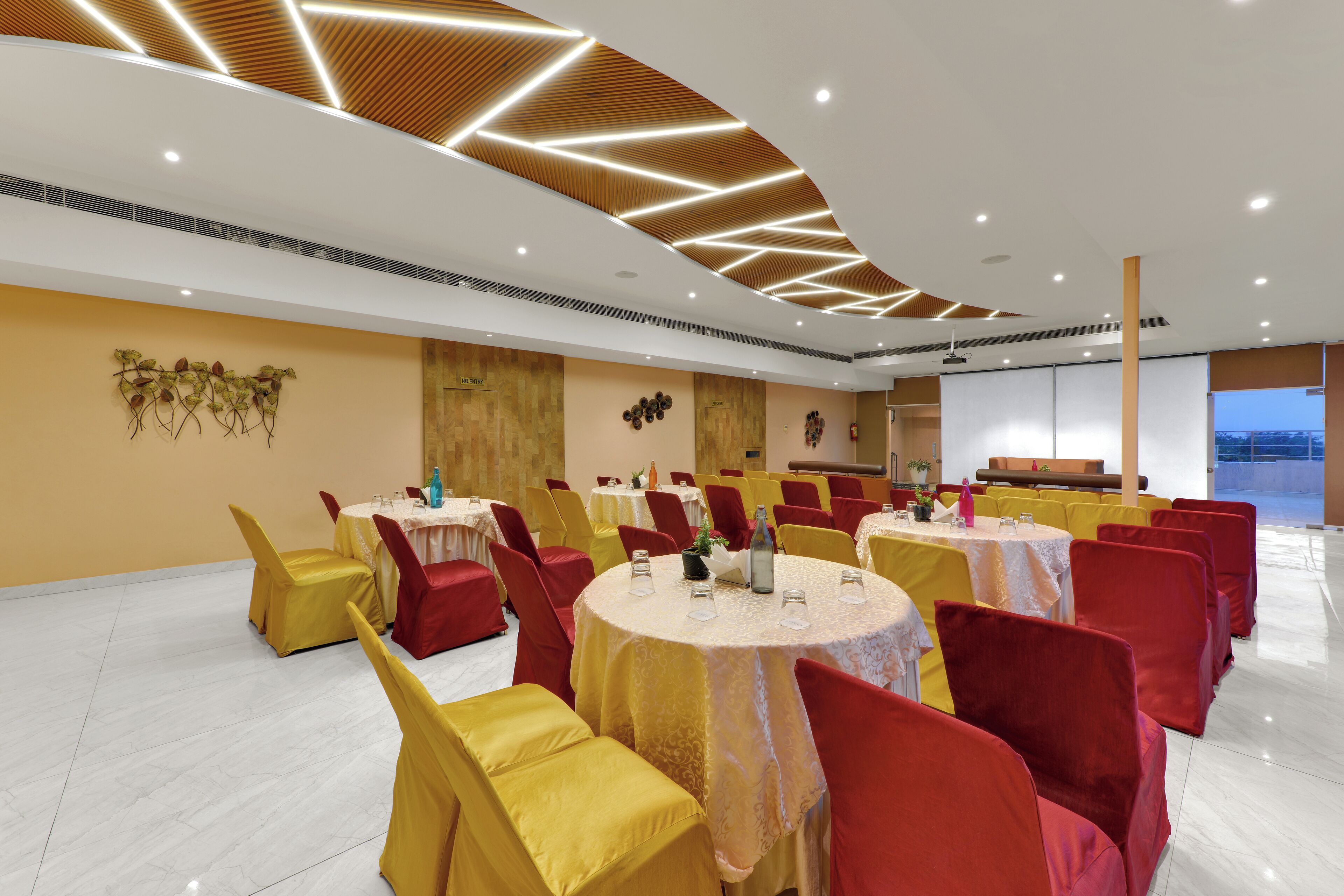 A banquet hall with round tables, red and yellow chairs, and a modern ceiling design.