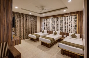 Habitación de hotel con tres camas individuales, cabecera de madera, televisor de pantalla plana y ventilador de techo.