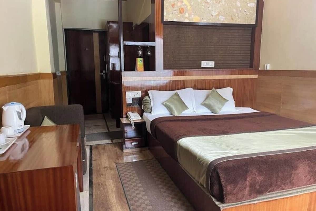 A hotel room with a wooden bed, a desk with a kettle, a telephone, and a small cabinet.