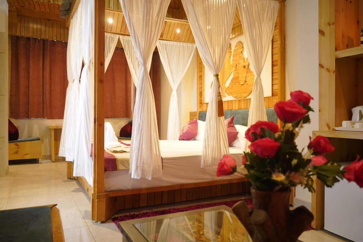 A four-poster bed with white drapes, a wooden headboard, and a bedside table with a vase of red roses.