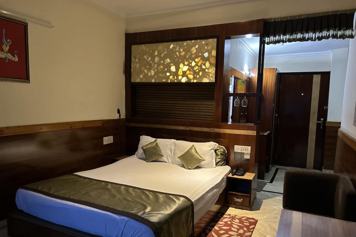 A hotel room with a large bed, a bedside table with a lamp, a mirror, and a door leading to another room.