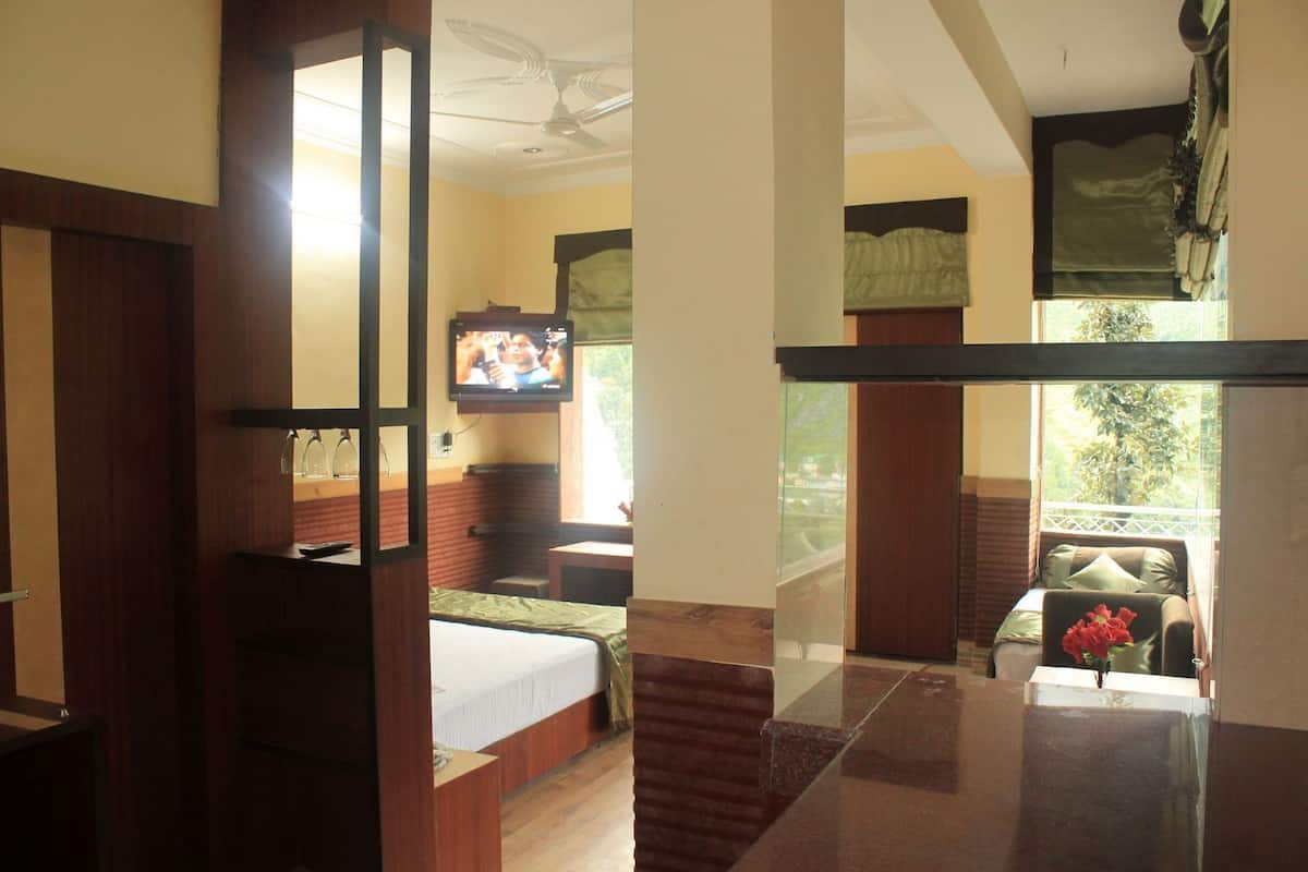 A hotel room with a bed, a TV, a balcony with a chair, and a view of greenery.
