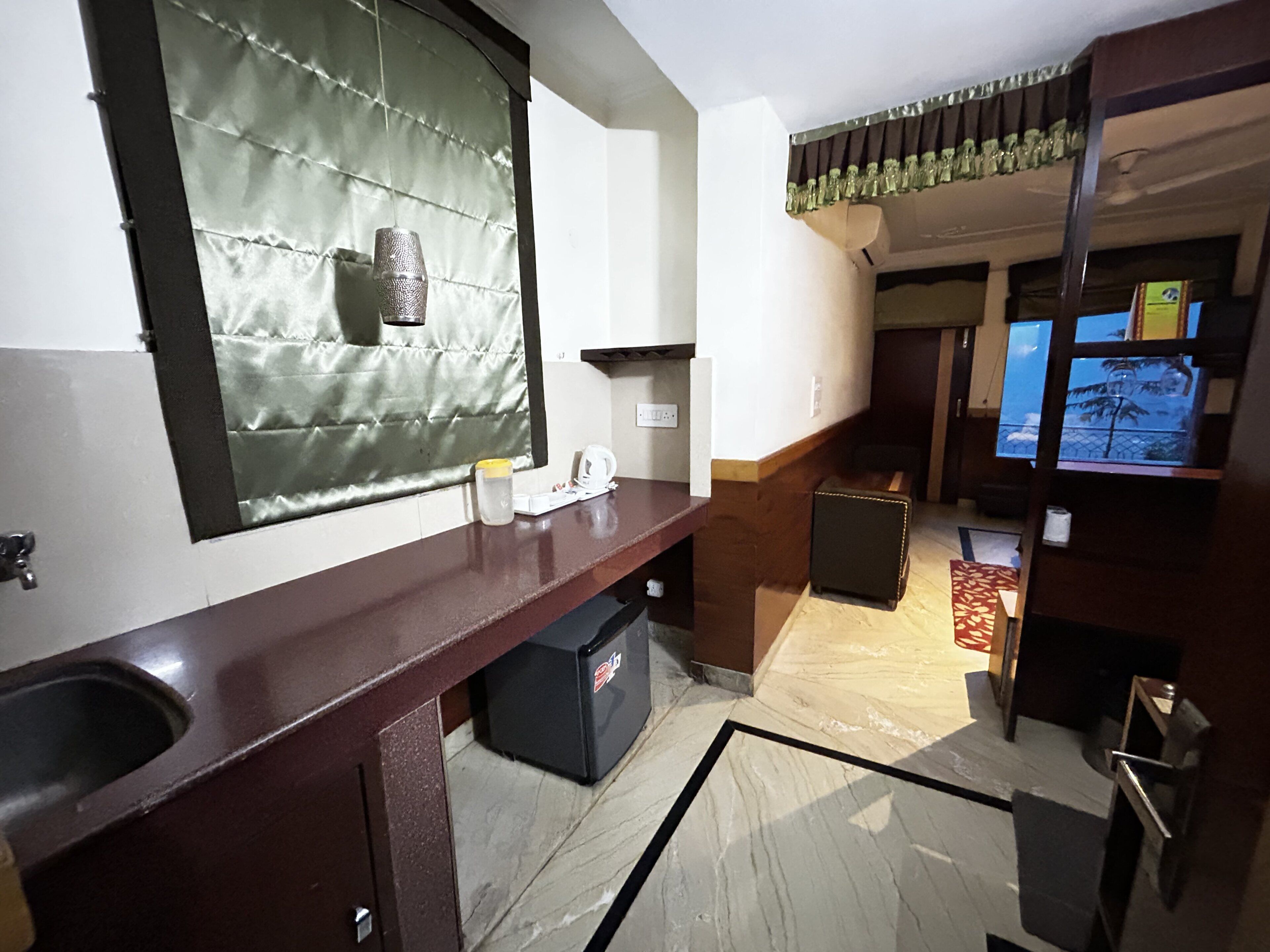 A hotel room with a large mirror, a sink, a small refrigerator, and a view of the outside balcony.