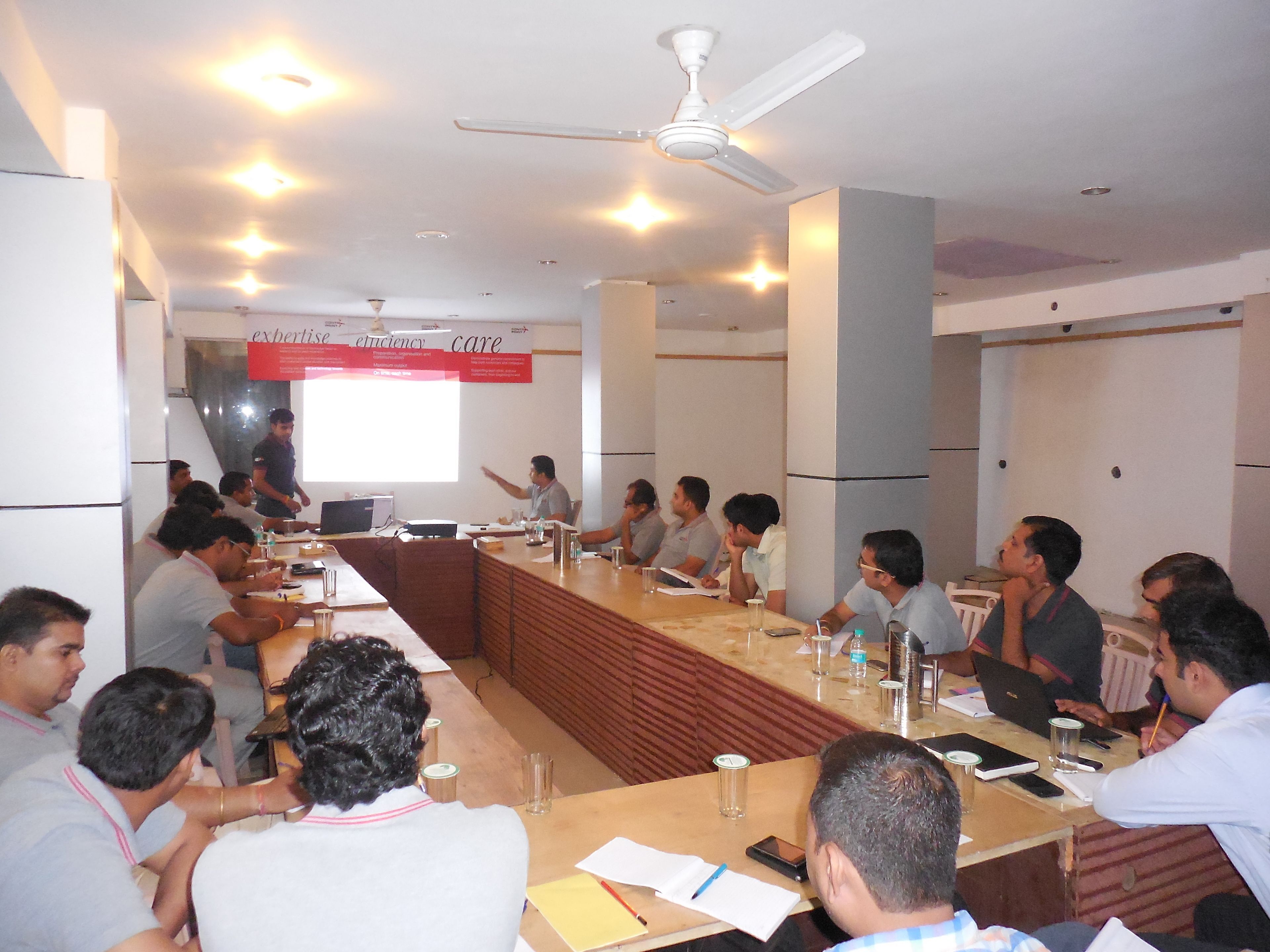 A conference room with a long table, attendees, and a presentation screen.