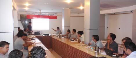 A conference room with a long table, attendees, and a presentation screen.
