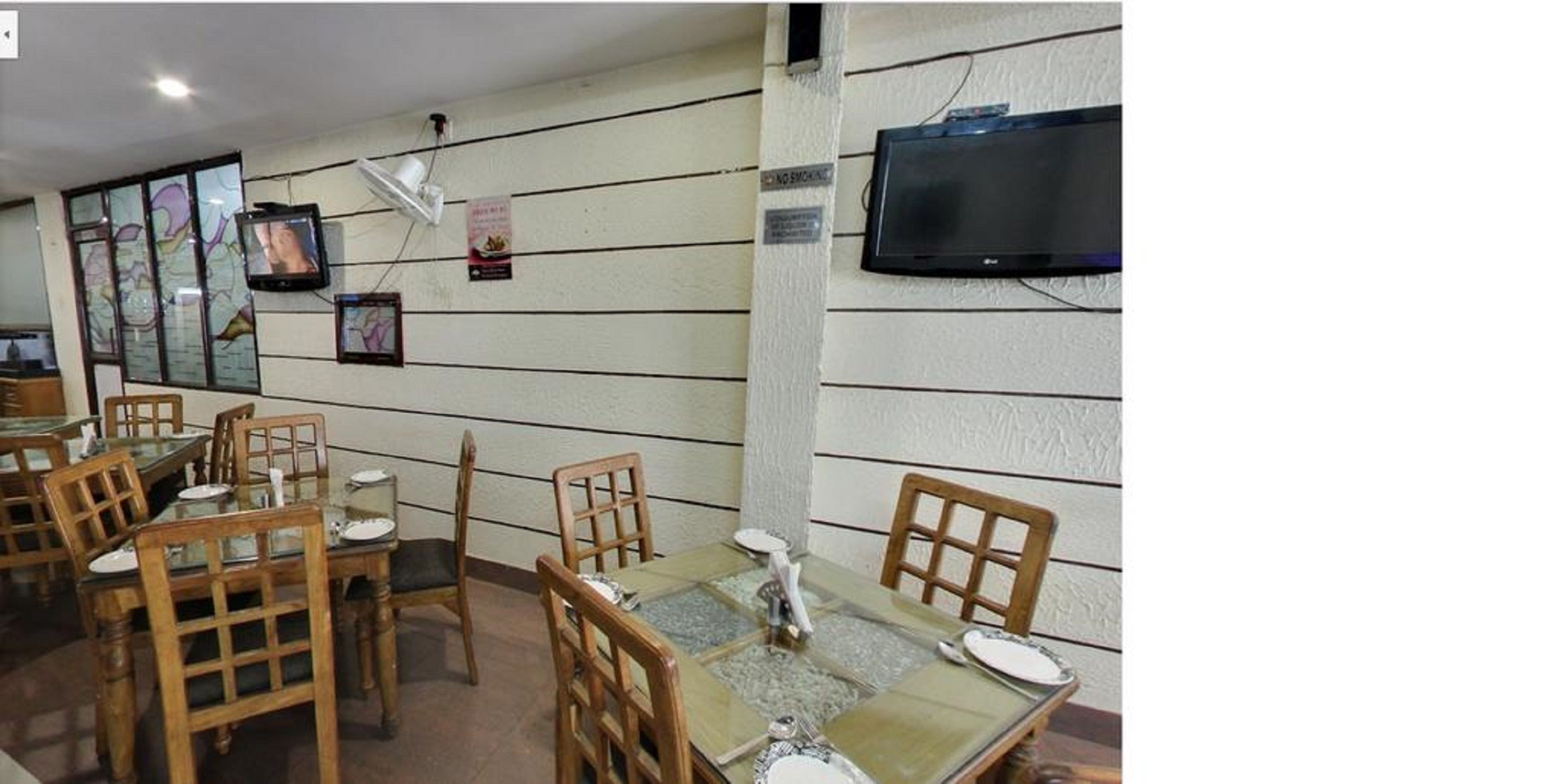 A dining area with wooden chairs and tables, a television mounted on the wall, and a sign indicating a smoking area.