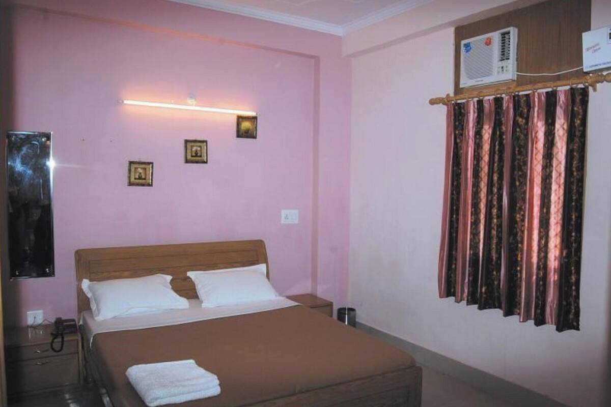 A bedroom with a bed, bedside tables, a wall-mounted air conditioner, and a curtain.