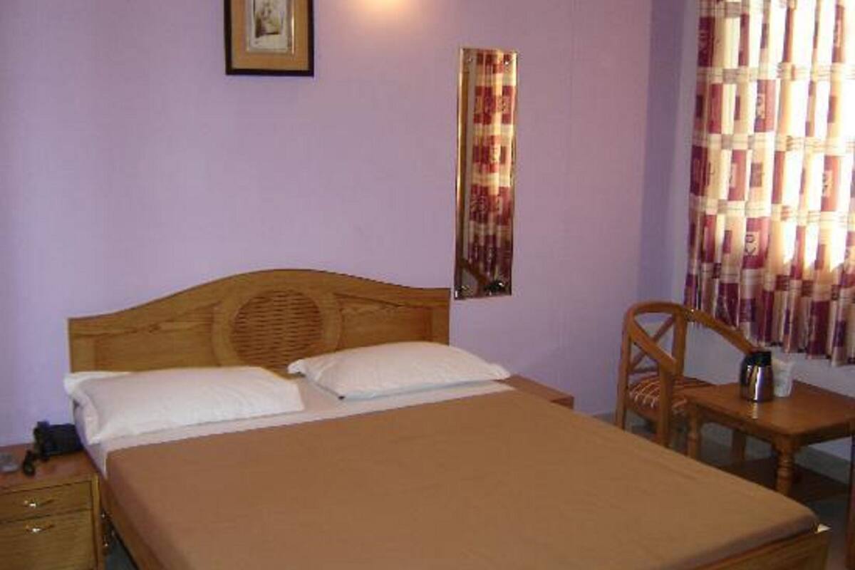 A single bed with a wooden headboard, a bedside table, a chair, and a small table with a cup.