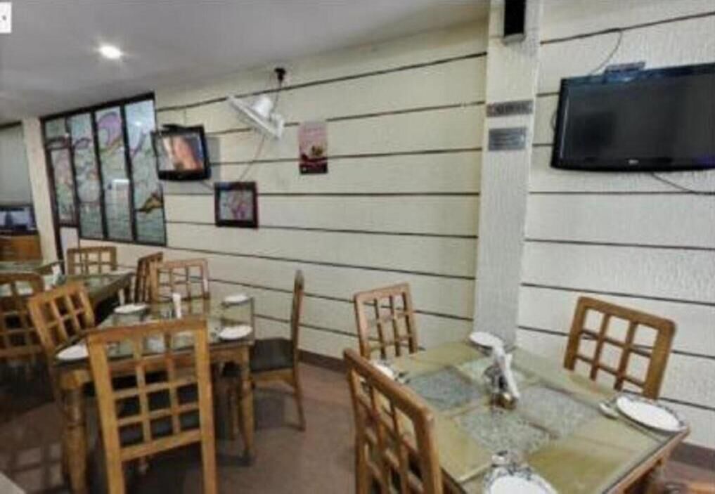 A dining area with wooden chairs and tables, a flat-screen TV mounted on the wall, and framed pictures on the wall.