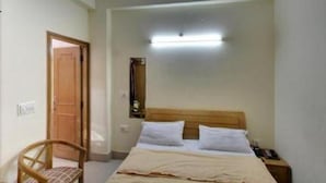 A small, simple room with a bed, a chair, and a nightstand. - Hotel Landmark-Haridwar (Haridwar)