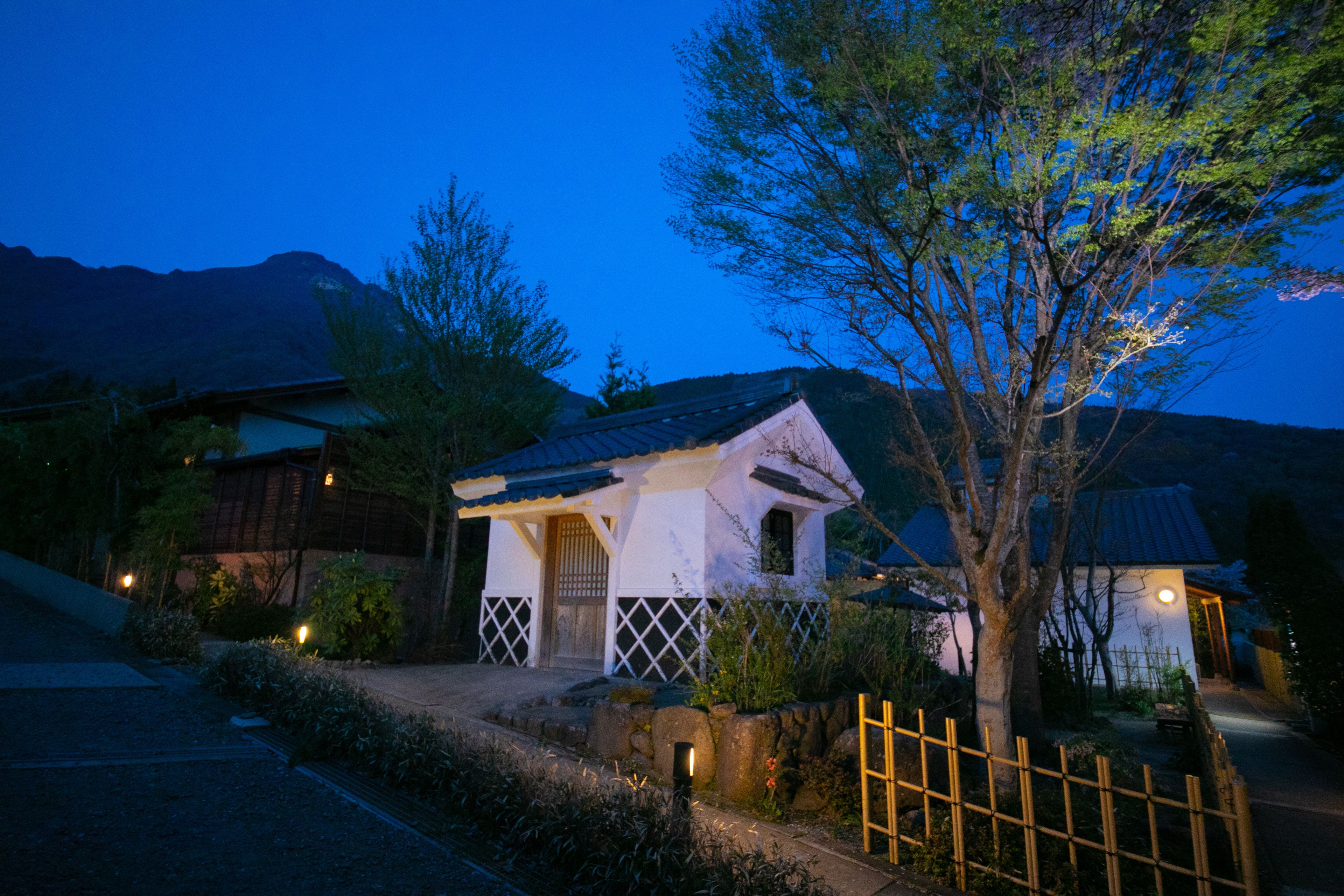 Una casa tradicional japonesa con un portón de madera, rodeada por un muro de piedra y una valla de bambú.