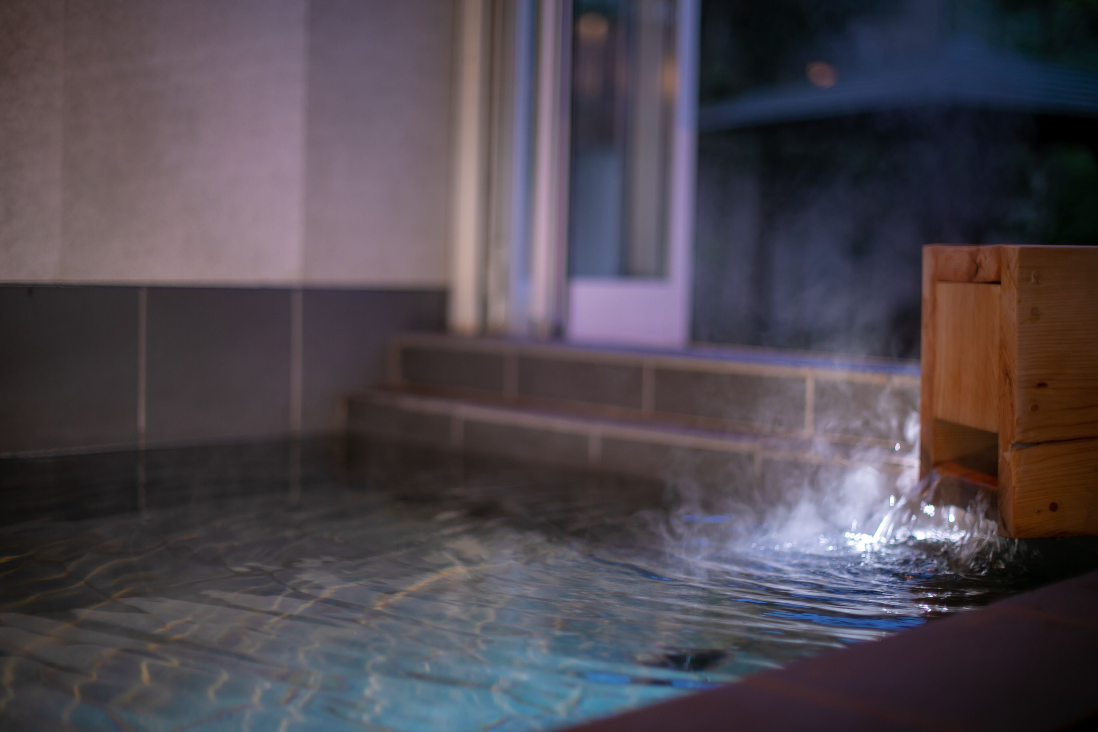 A hot tub with water flowing out, a wooden bench, and tiled flooring.
