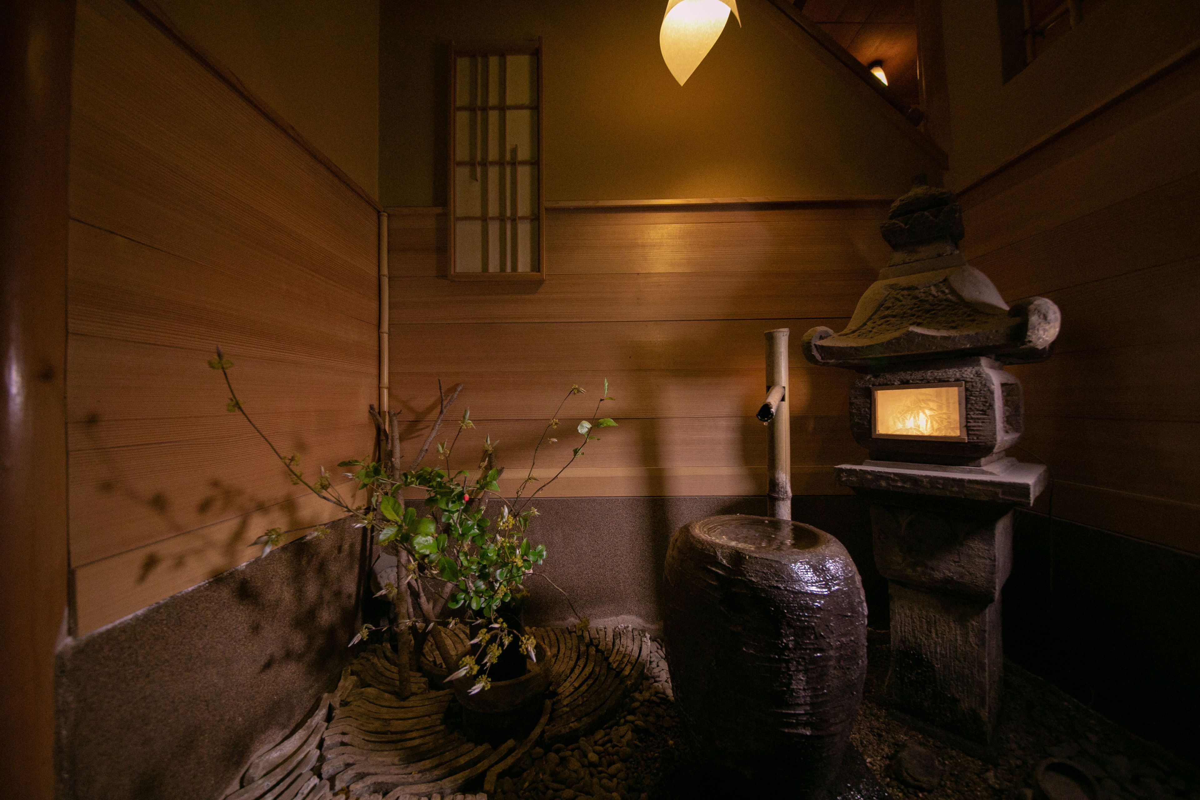 A traditional Japanese room with wooden walls, a stone lantern, and a potted plant.
