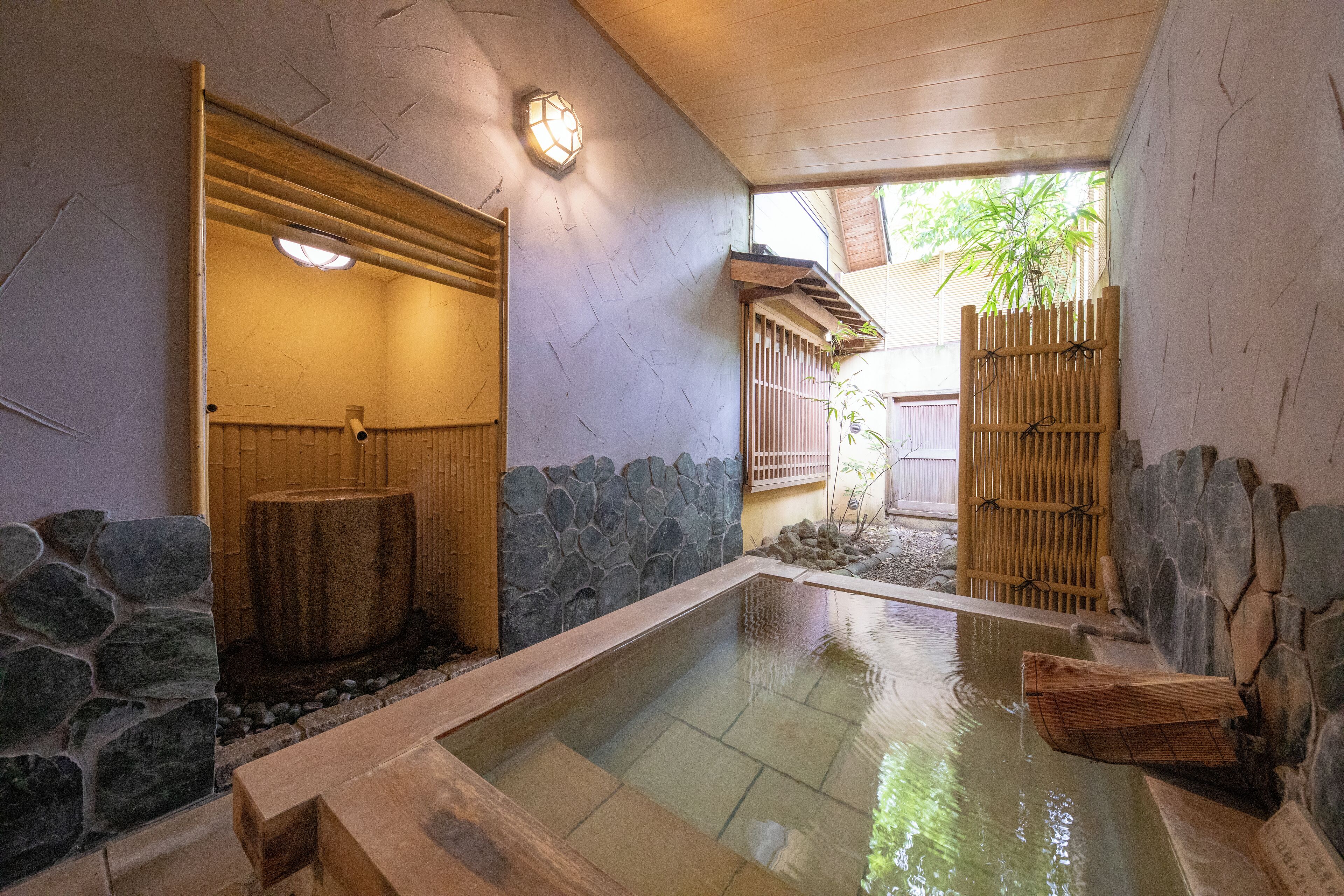A traditional Japanese onsen with a stone and wooden bath, a wooden walkway, and a bamboo fence.
