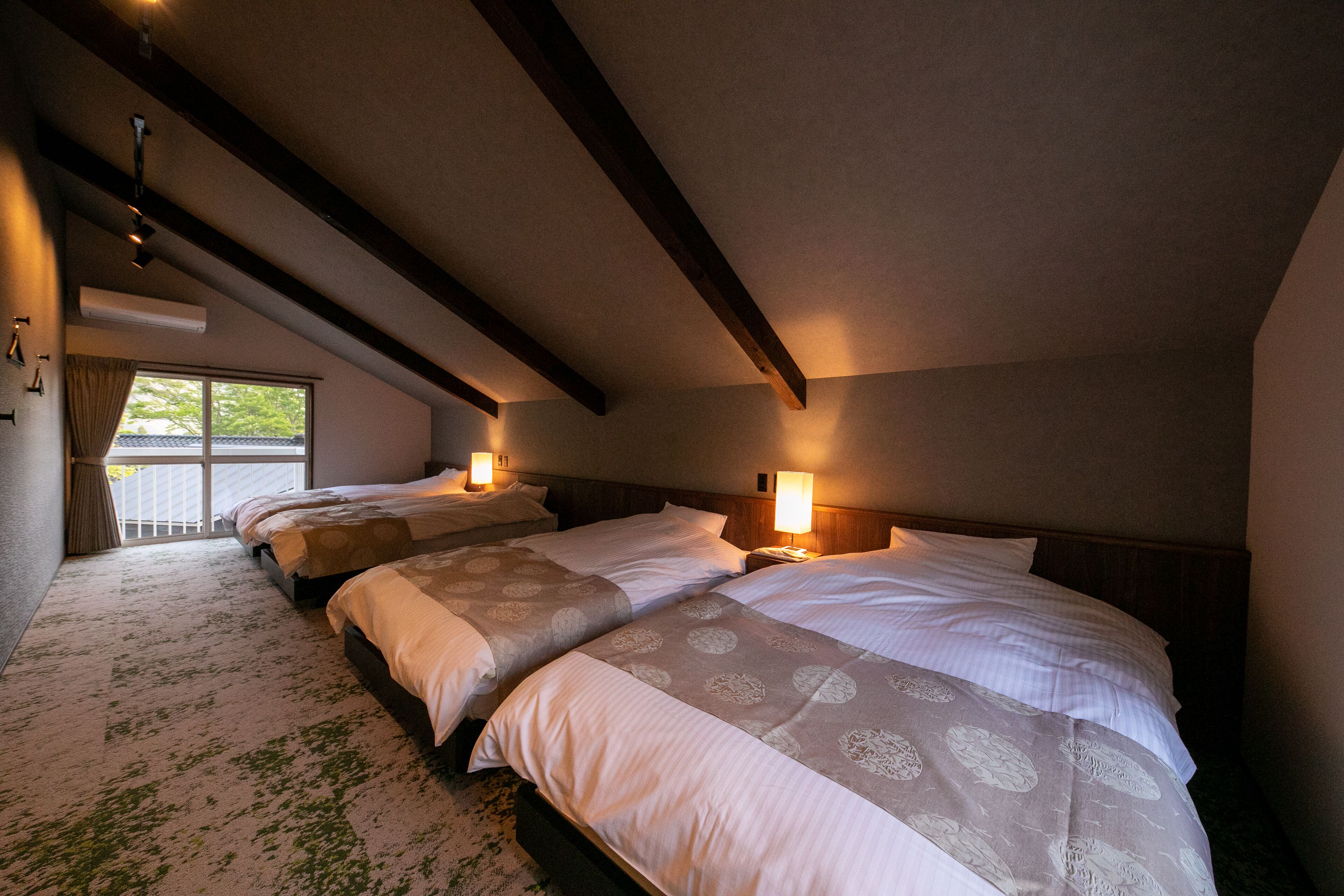 Habitación de hotel con tres camas, un ventanal grande y un techo inclinado.