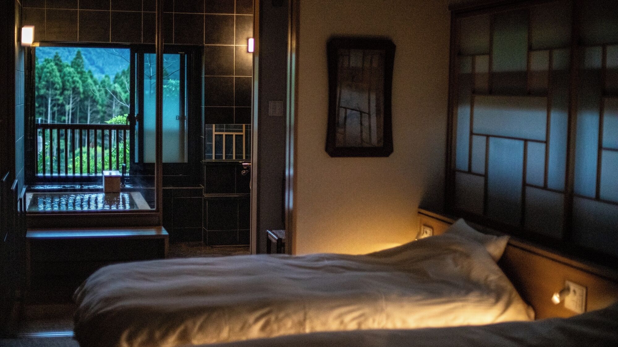A bedroom with a bed, a window with a view of trees, and a small table.