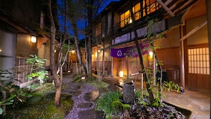 A traditional Japanese-style courtyard with stone pathways, bamboo plants, and a wooden building with illuminated windows. - Oyado Ichizen (Yufu)