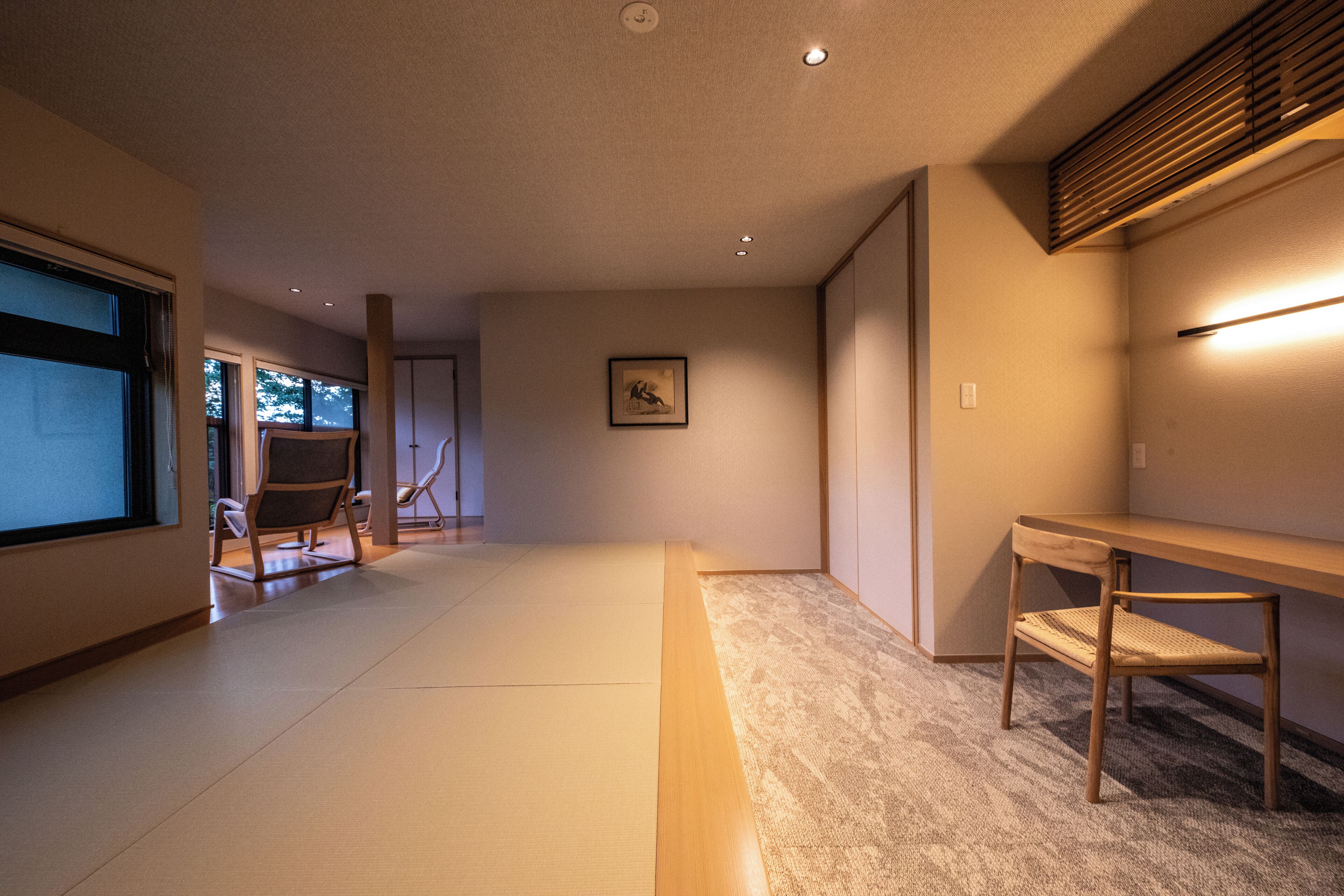 A spacious room with tatami flooring, a low wooden table, and a chair.