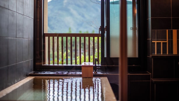 A traditional Japanese onsen with a wooden bench and a view of a mountain through a sliding door. - Oyado Ichizen (Yufu)