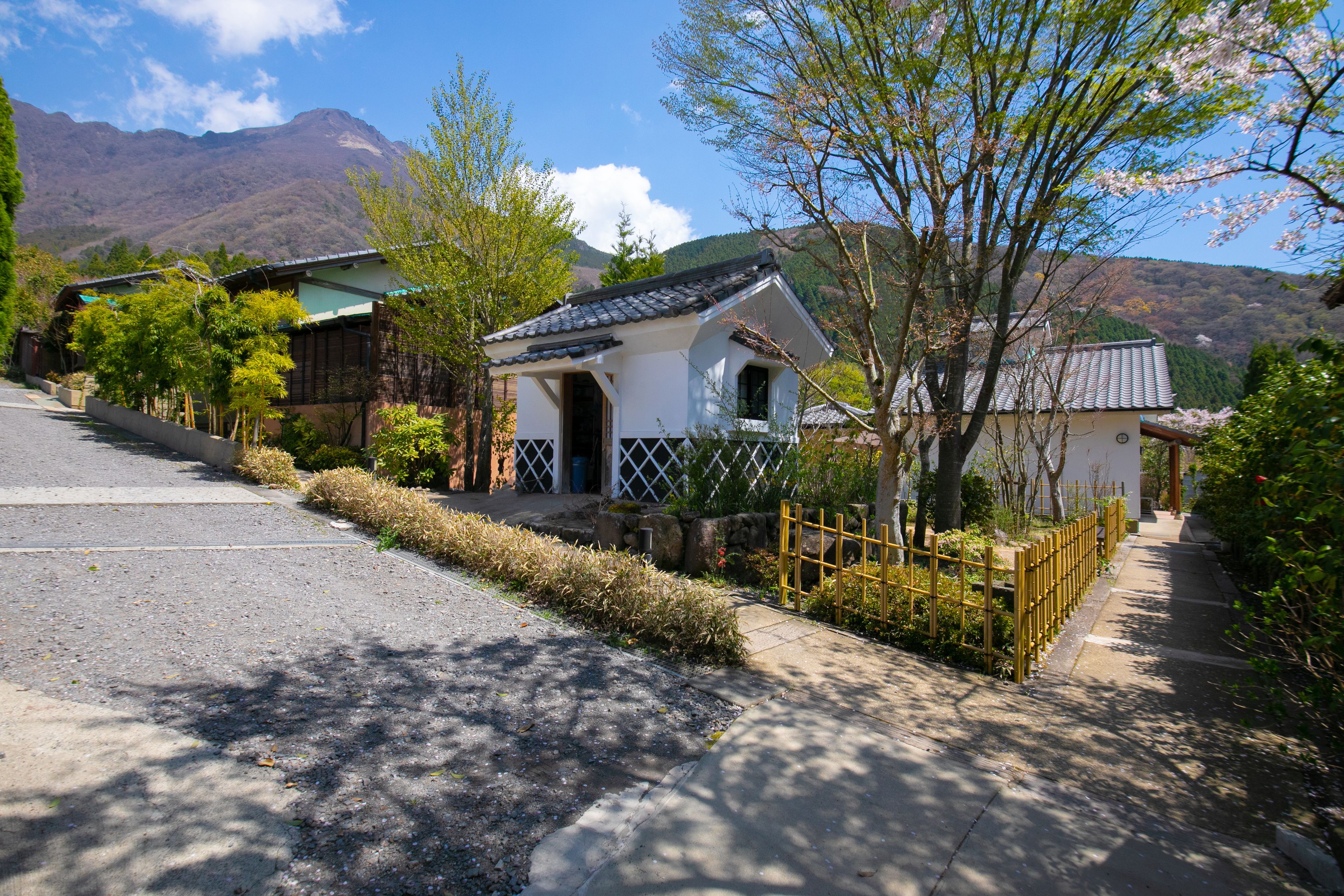 A traditional Japanese house with a tiled roof, surrounded by greenery and mountains in the background.