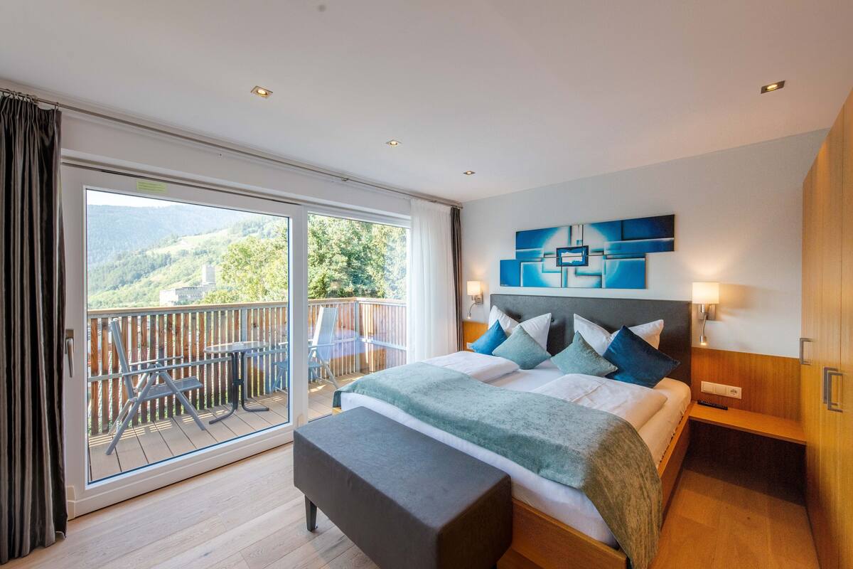 A modern hotel room with a large sliding glass door leading to a balcony with outdoor furniture.