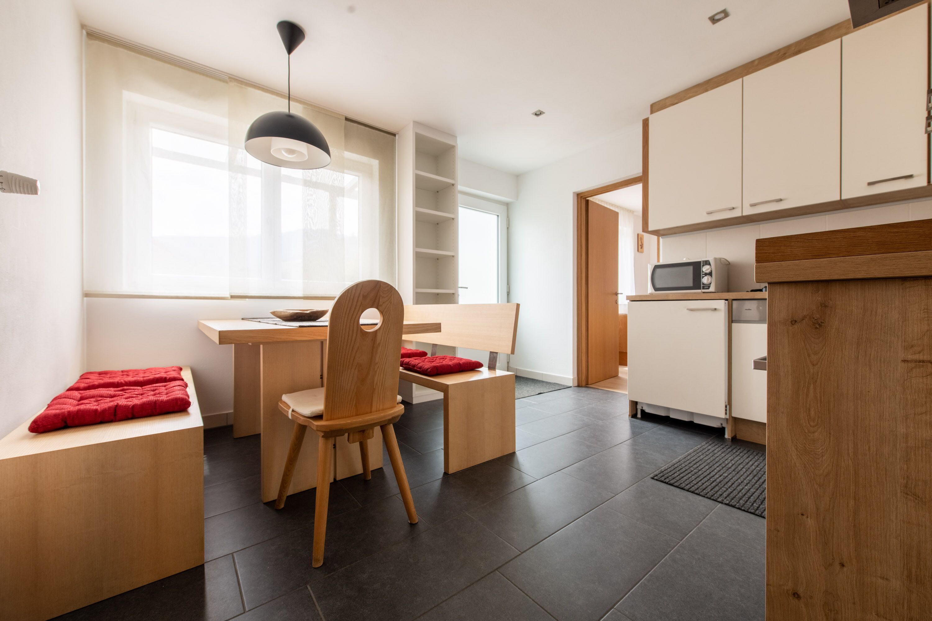 Una cocina moderna con armarios blancos, microondas y comedor con mesa y sillas de madera.