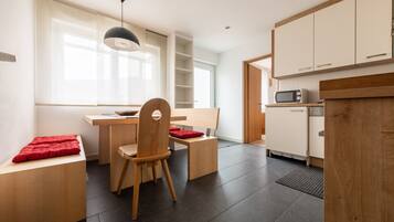Una cocina moderna con armarios blancos, microondas y comedor con mesa y sillas de madera.
