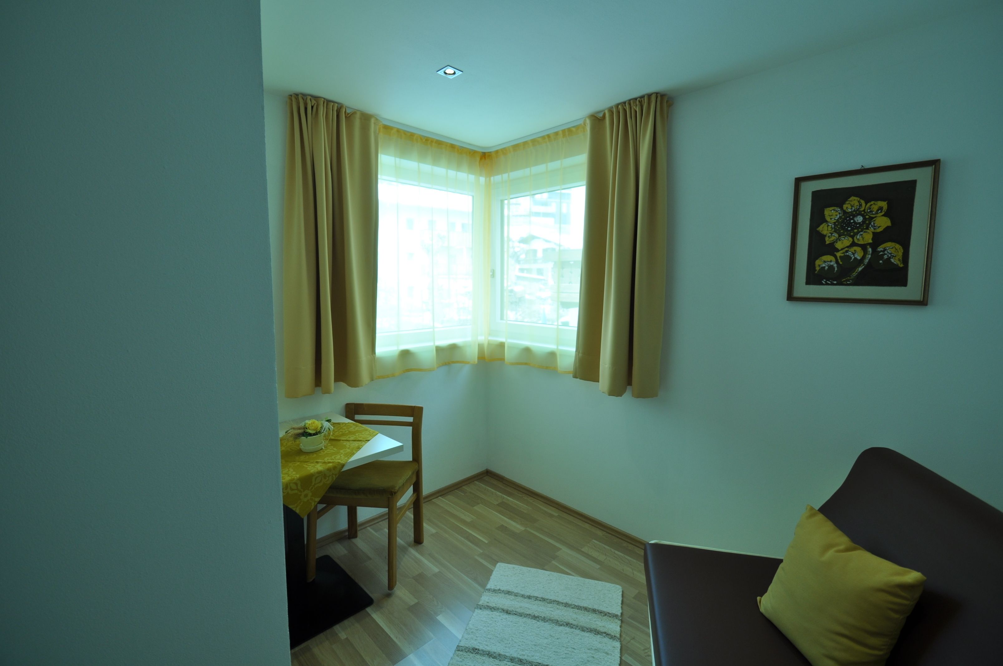Ein Eckzimmer mit Esstisch, einem Sessel, einer Couch und einem fenster mit Vorhängen.