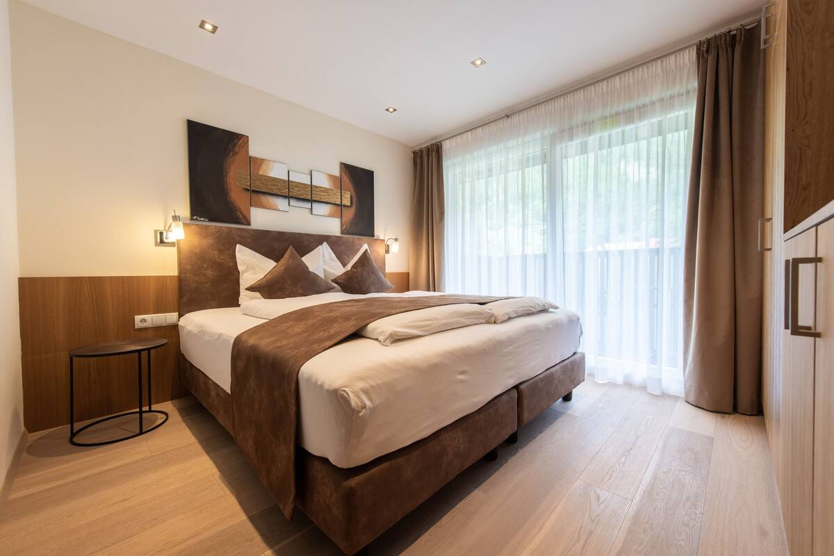 A modern hotel room with a large bed, a bedside table, and a window with curtains.