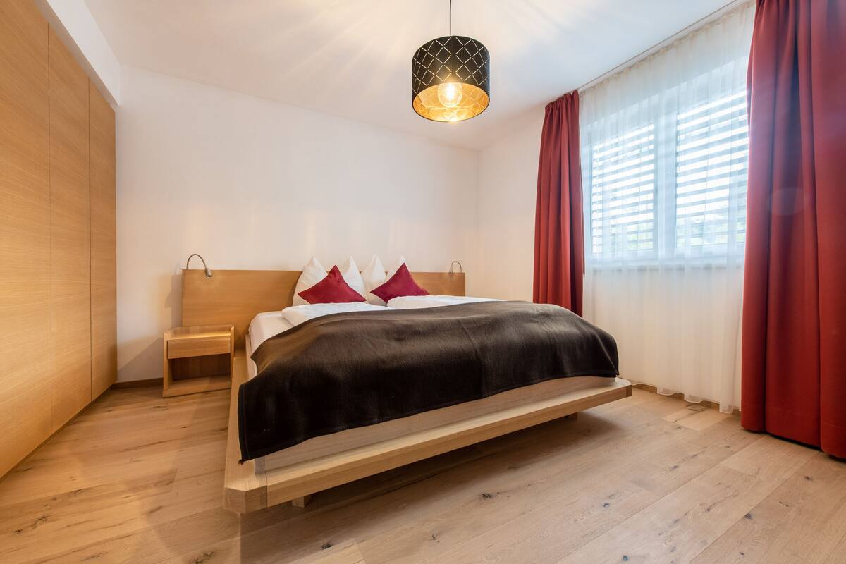 A modern bedroom with a wooden bed, a bedside table, and a hanging light fixture.