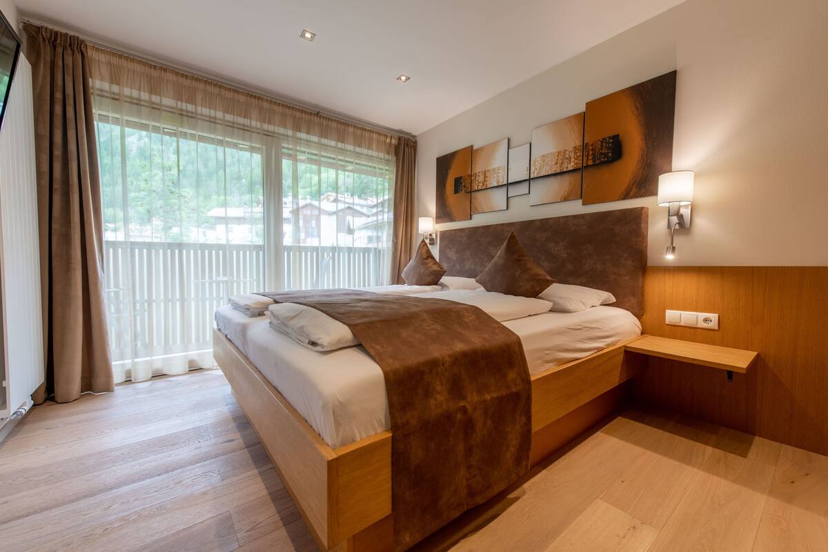 A modern bedroom with a large bed, wooden headboard, and a view of greenery outside.