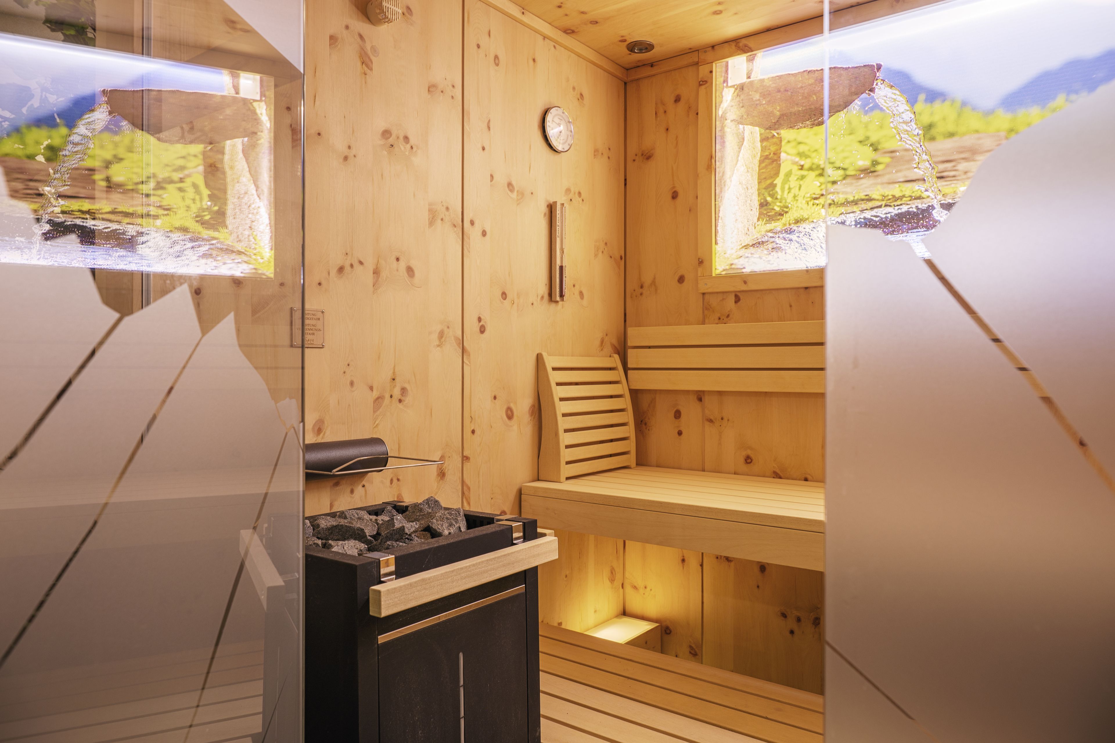 A wooden sauna with a wooden bench, a clock, and a window with a view of mountains.