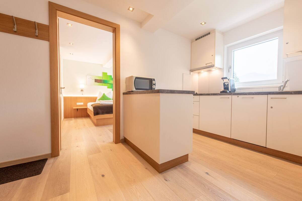 A modern kitchen with wooden flooring, white cabinets, and a microwave on the counter.
