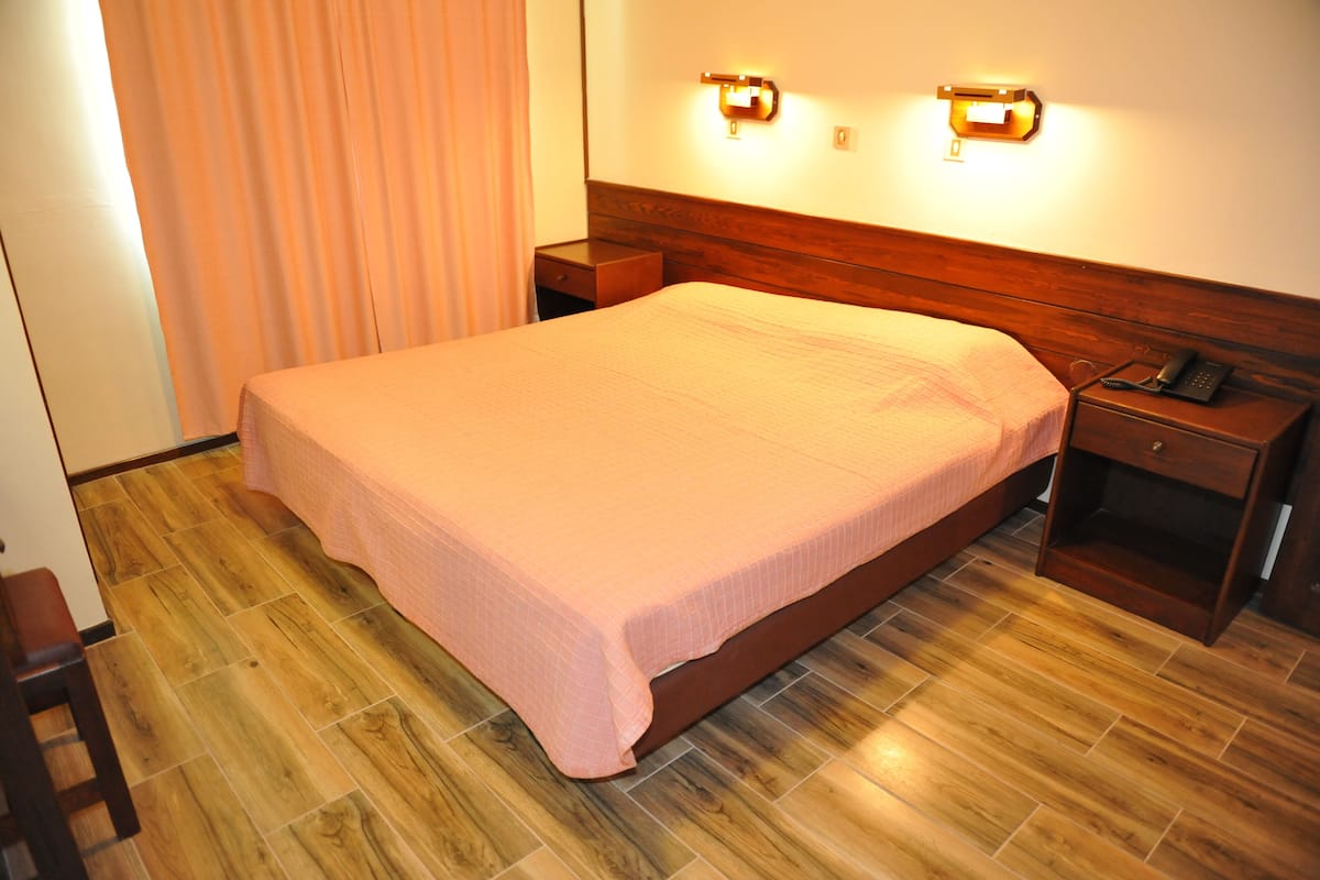 Ein Hotelzimmer mit einem hölzernen Bett, einem Nachttisch mit Telefon und einer an der Wand befestigten Leuchte.