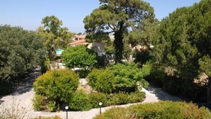 A landscaped garden with various trees and shrubs, a pathway, and a building with a red roof in the background. - Niki Hotel Apartments (Rhodes)