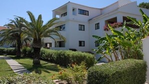 A modern multi-story building with a white facade, surrounded by well-maintained gardens and palm trees. - Niki Hotel Apartments (Rhodes)
