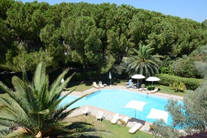 A swimming pool surrounded by lounge chairs and umbrellas, with a dense forest in the background. - Niki Hotel Apartments (Rhodes)