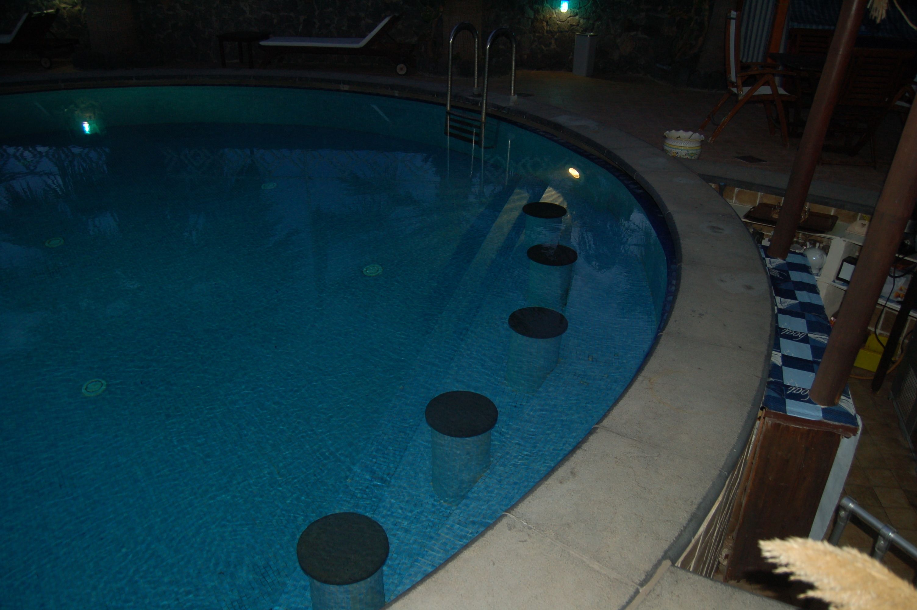 Una piscina con escalones de acceso, rodeada por un muro de piedra y un suelo con diseño de cuadros.