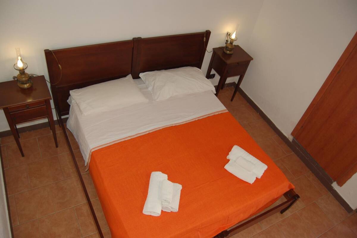 A single bed with an orange bedspread and white linens, two bedside tables with lamps, and a wooden headboard.