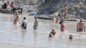 Une plage où l’on voit des gens dans l’eau et sur le rivage, certains portant des chapeaux et des maillots de bain.