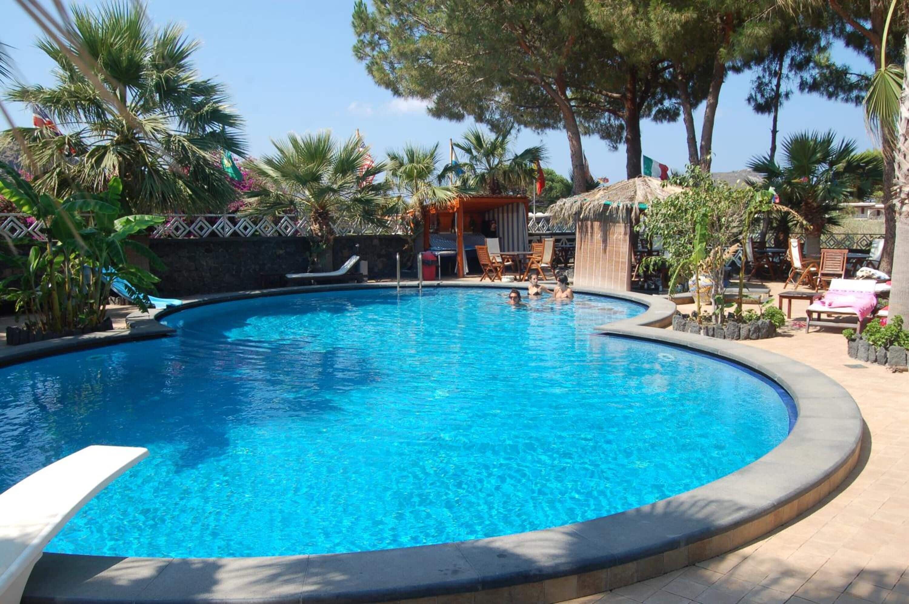 A swimming pool with a curved edge, surrounded by palm trees and lounge chairs.