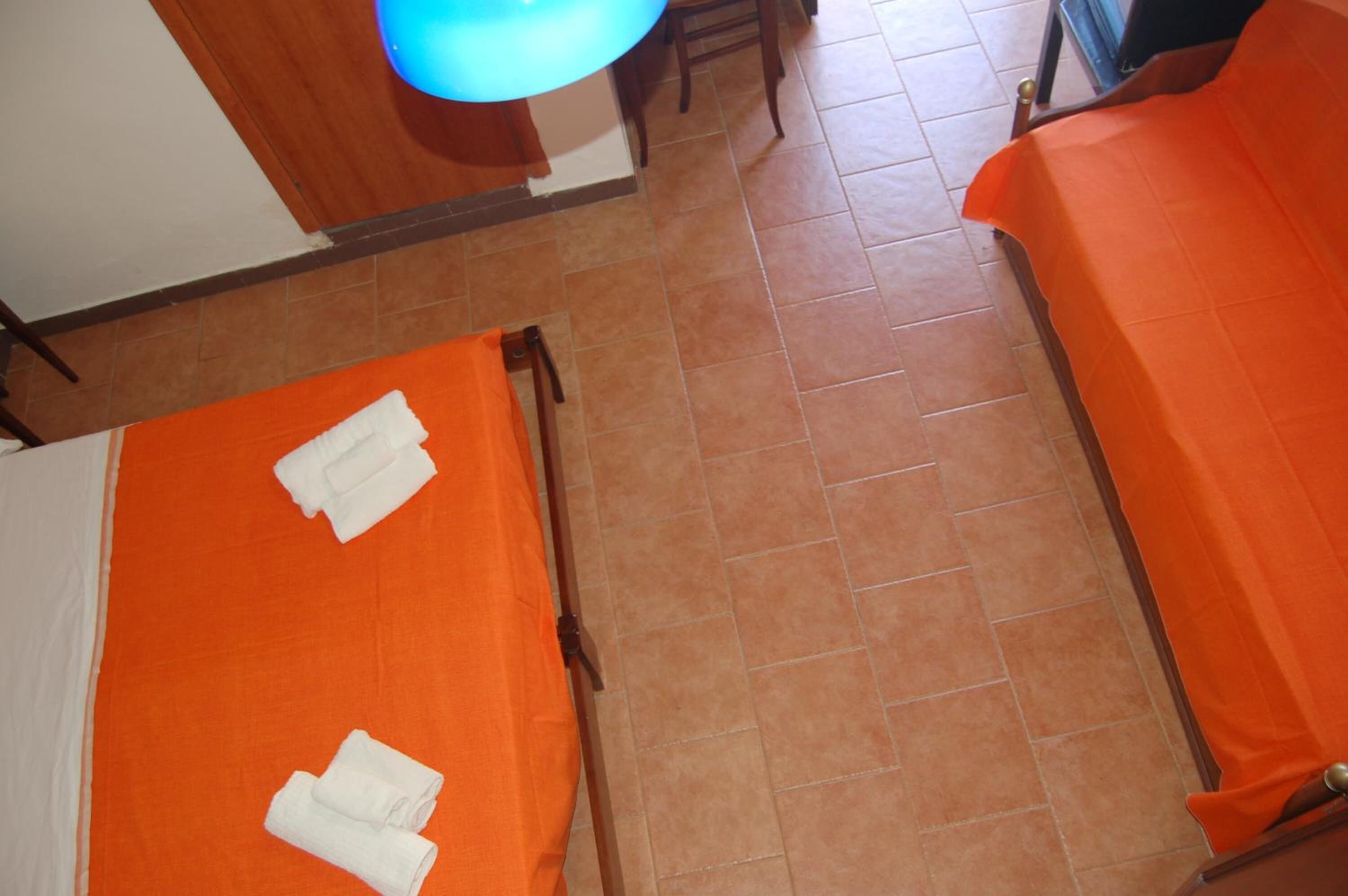 A hotel room with two beds covered in orange sheets, a wooden floor, and a blue light fixture above the beds.