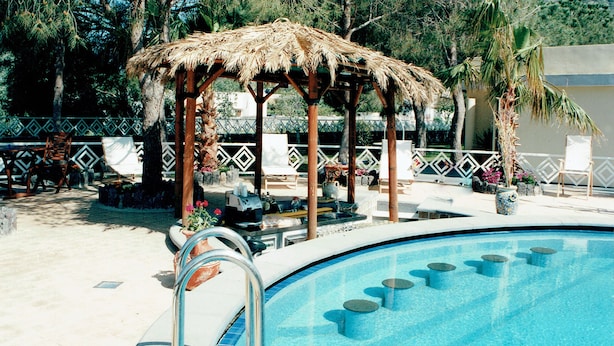 Un espace piscine agrémenté d’un gazebo à toit de chaume, de chaises longues et d’une piscine accessible par des marches.