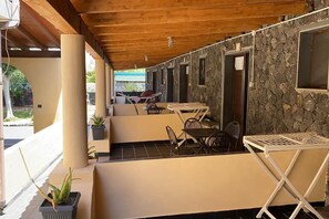 Uma área de estar coberta ao ar livre, com mesas e cadeiras, paredes de pedra e teto de madeira.