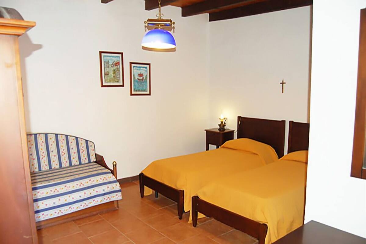 A bedroom with two beds, a sofa, a small table, and a cross on the wall.