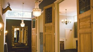 Un pasillo con puertas de madera, un espejo con un marco decorativo y candelabros.